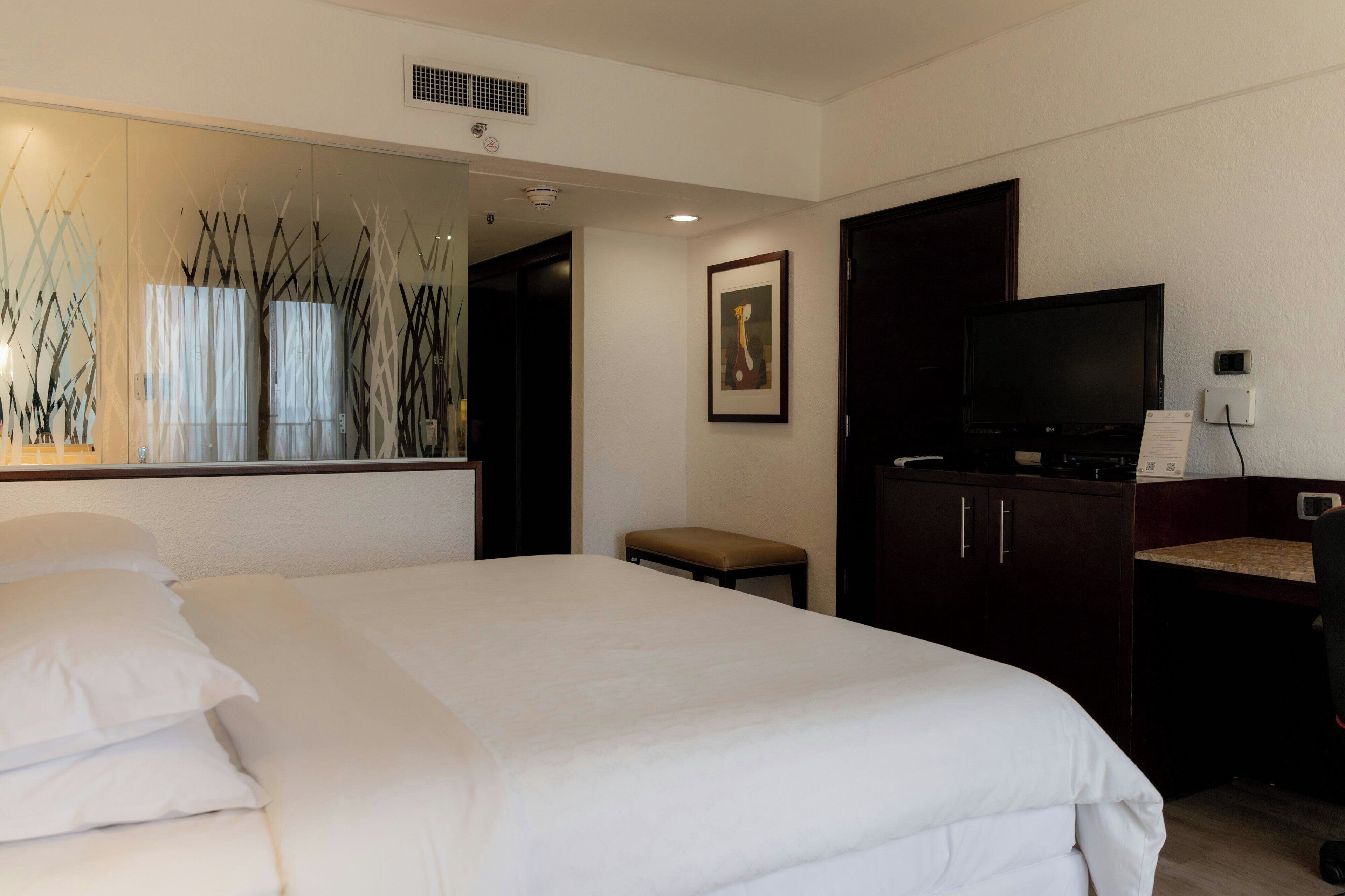 Une chambre d’hôtel avec un grand lit, un bureau avec une chaise, une télévision et un miroir.