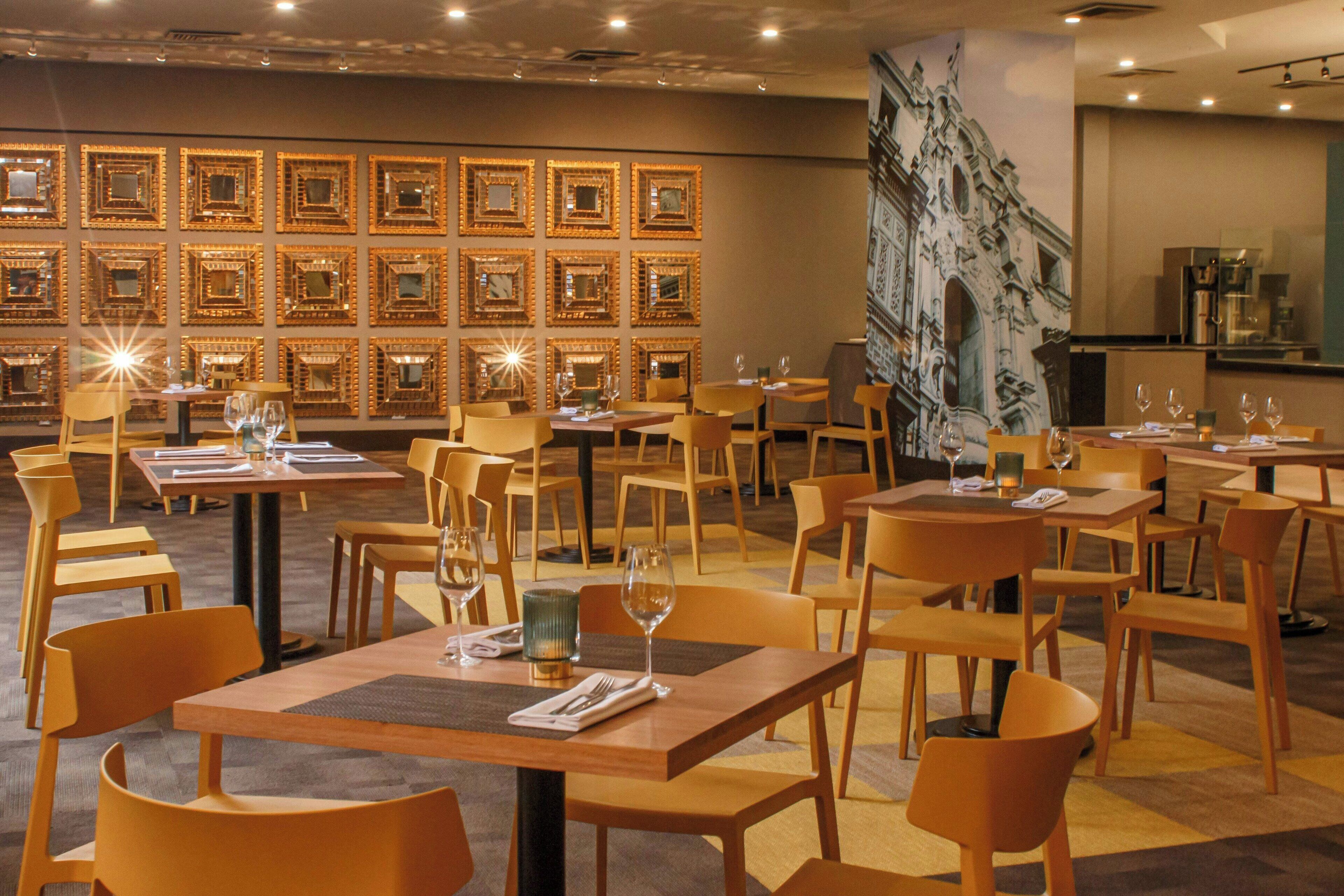 Un restaurante con varias mesas y sillas, un mural en la pared y una zona de cocina al fondo.