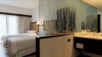 A hotel room with two beds, a large mirror, a modern bathroom with a sink and towel rack.