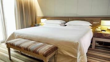 Une chambre d’hôtel avec un grand lit, une table de chevet avec une lampe, un banc et une fenêtre avec des rideaux.