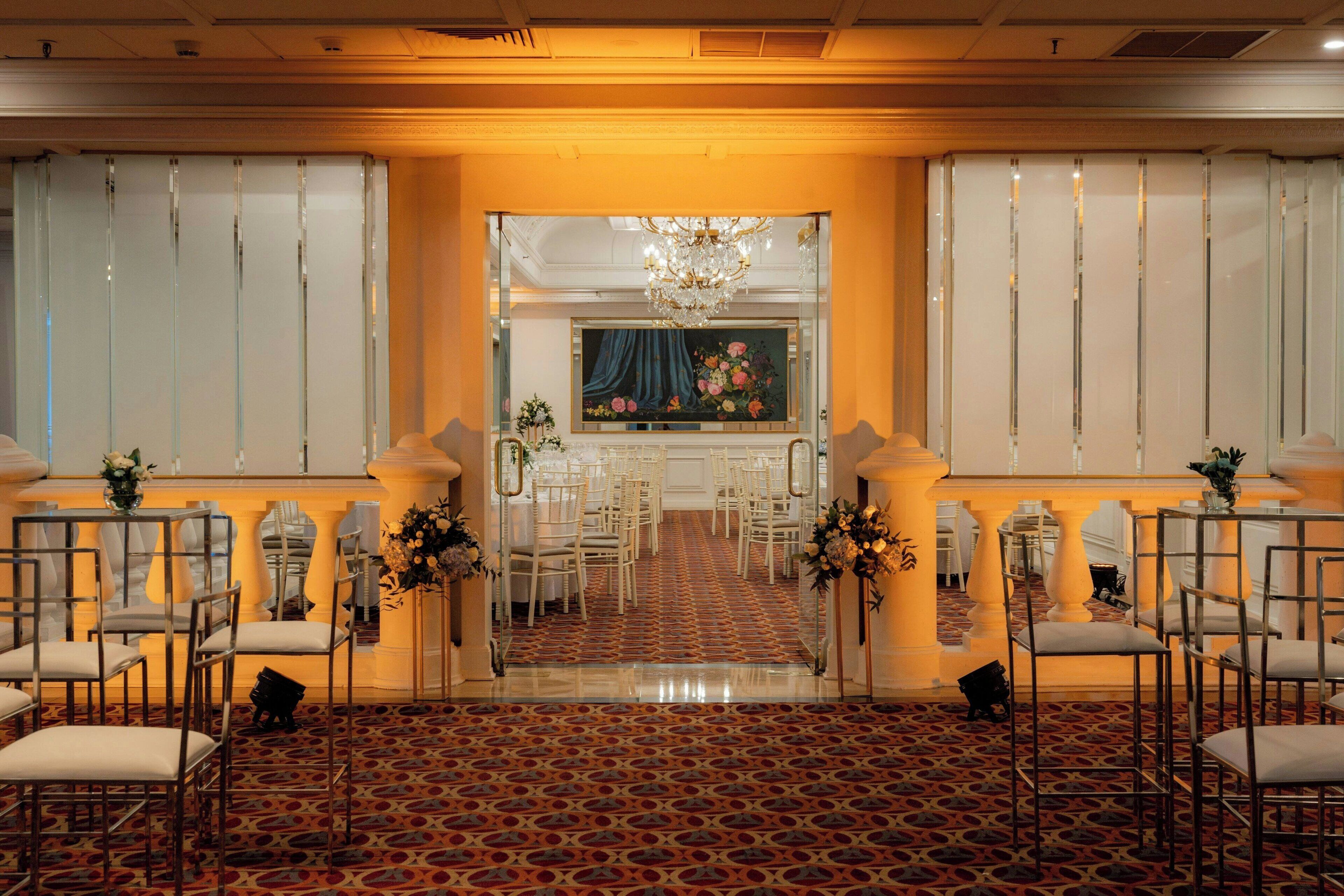 Un espacio para eventos formales, con alfombra estampada, filas de sillas, un pasillo central y un cuadro decorativo en la pared de fondo.