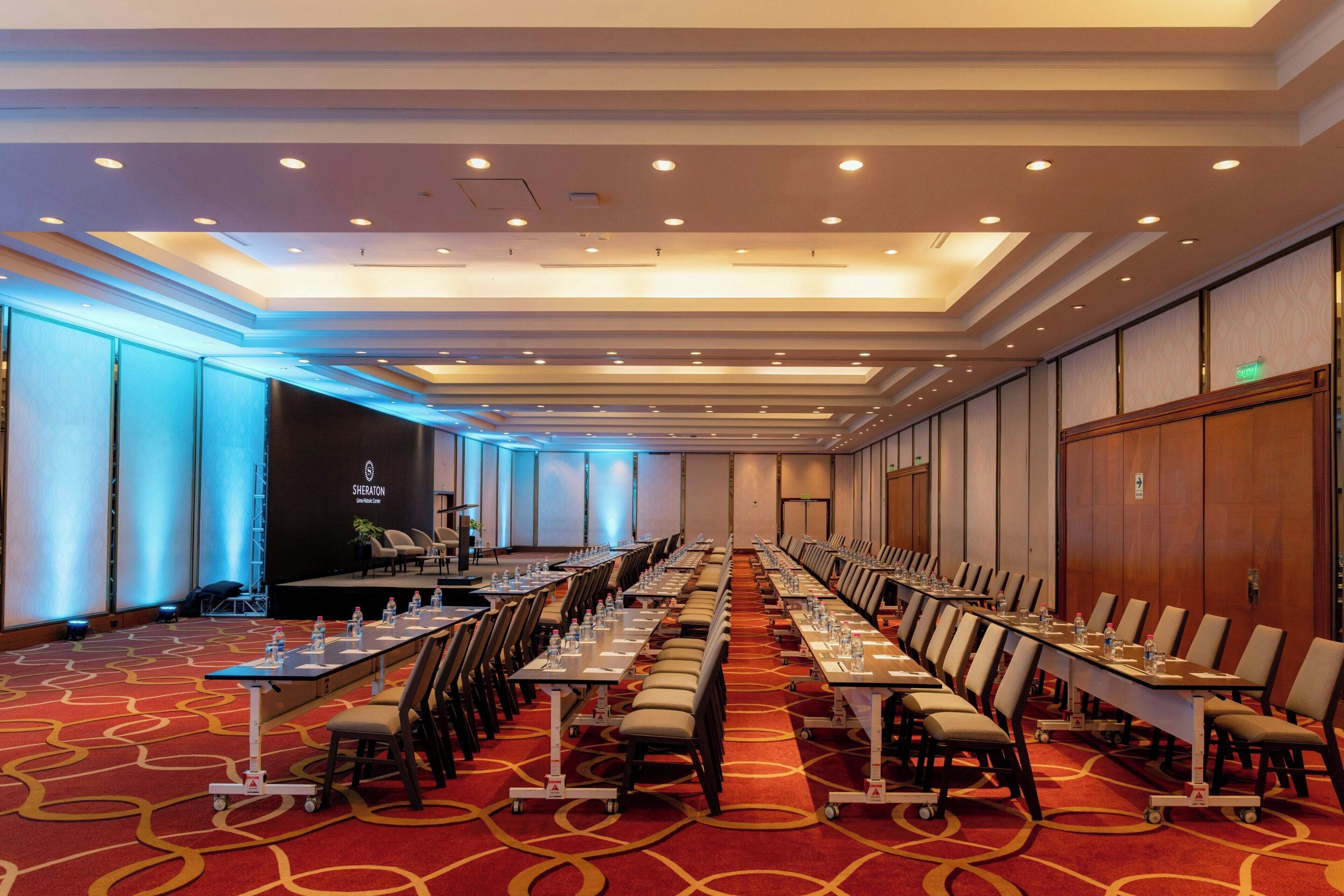 A conference room with rows of tables and chairs, a stage, and a Sheraton logo on the wall.