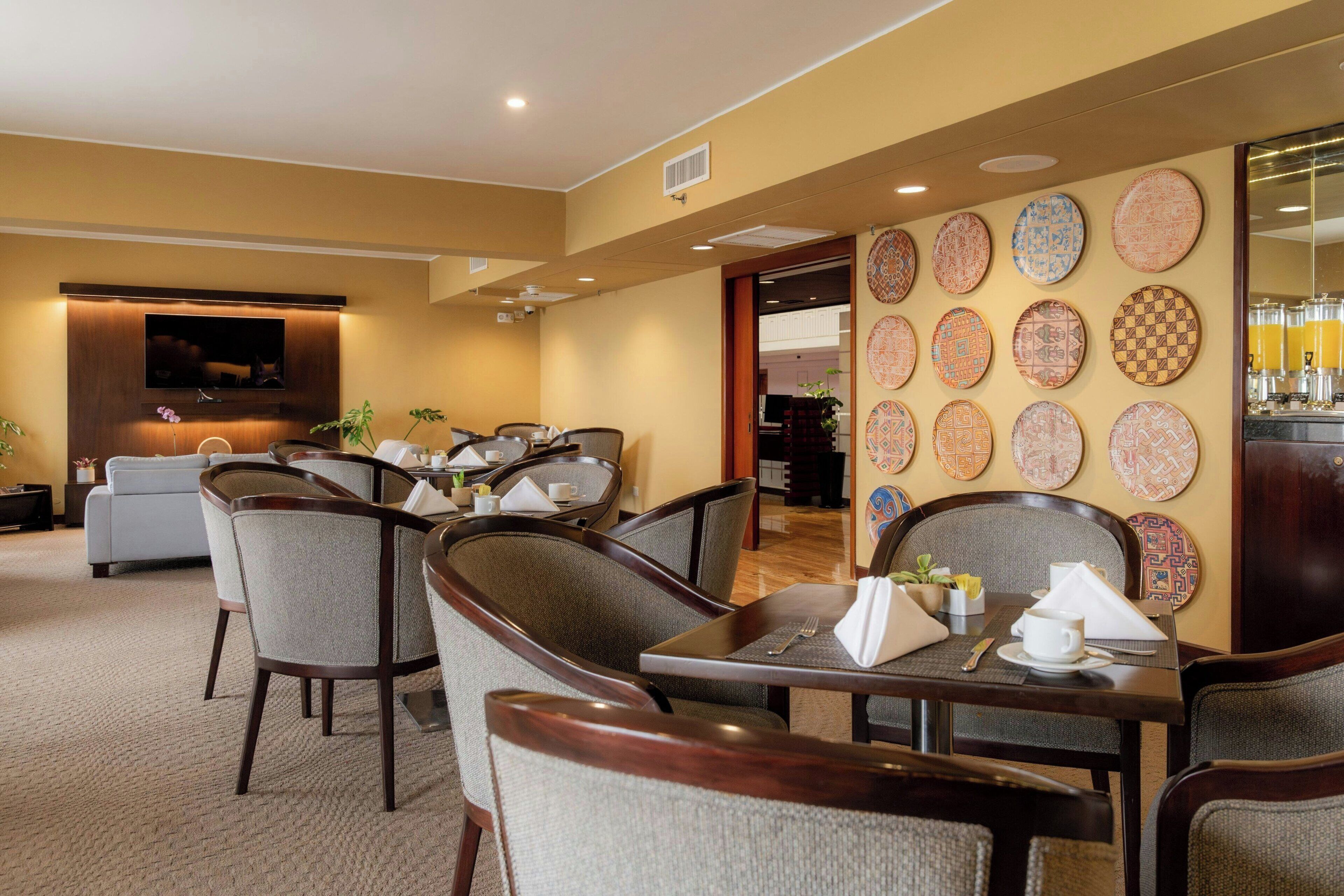 A dining area with multiple tables and chairs, a television mounted on the wall, and a wall decorated with circular plates.