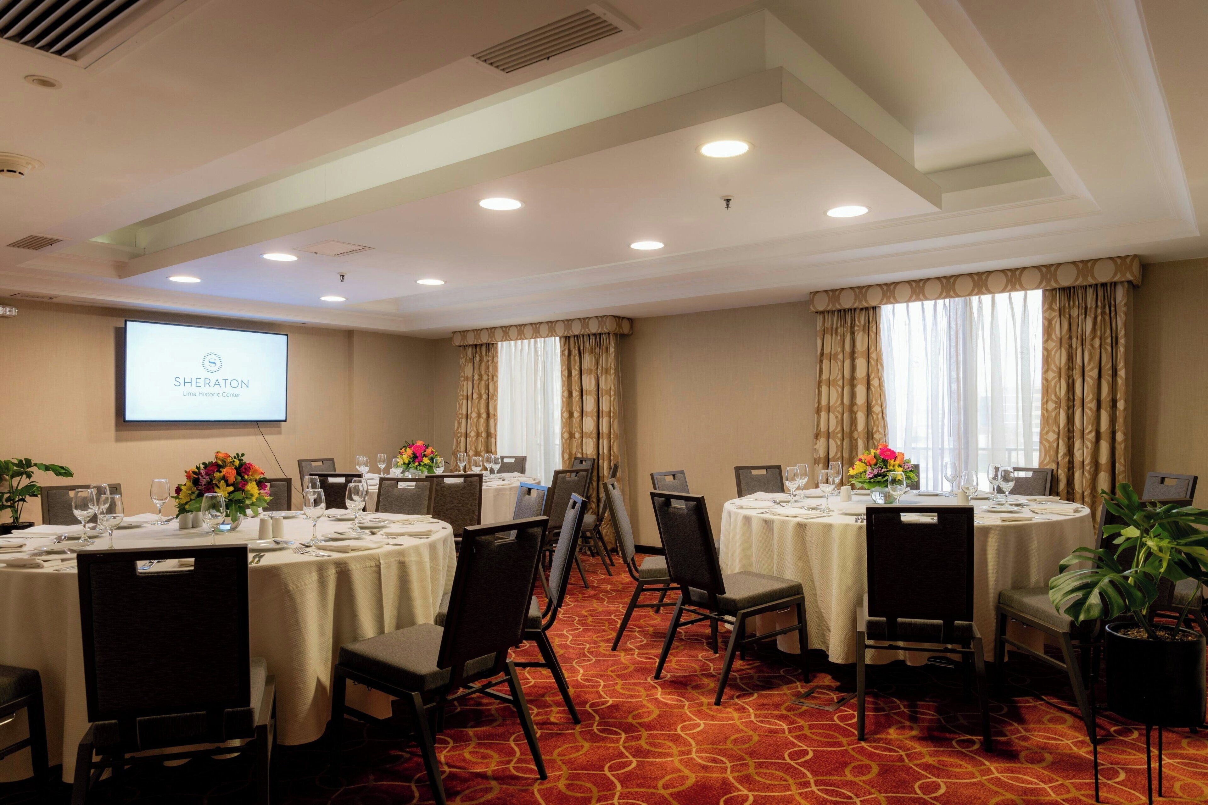 A conference room with multiple tables, chairs, and a projector screen displaying 'SHERATON Lima Historic Center'.