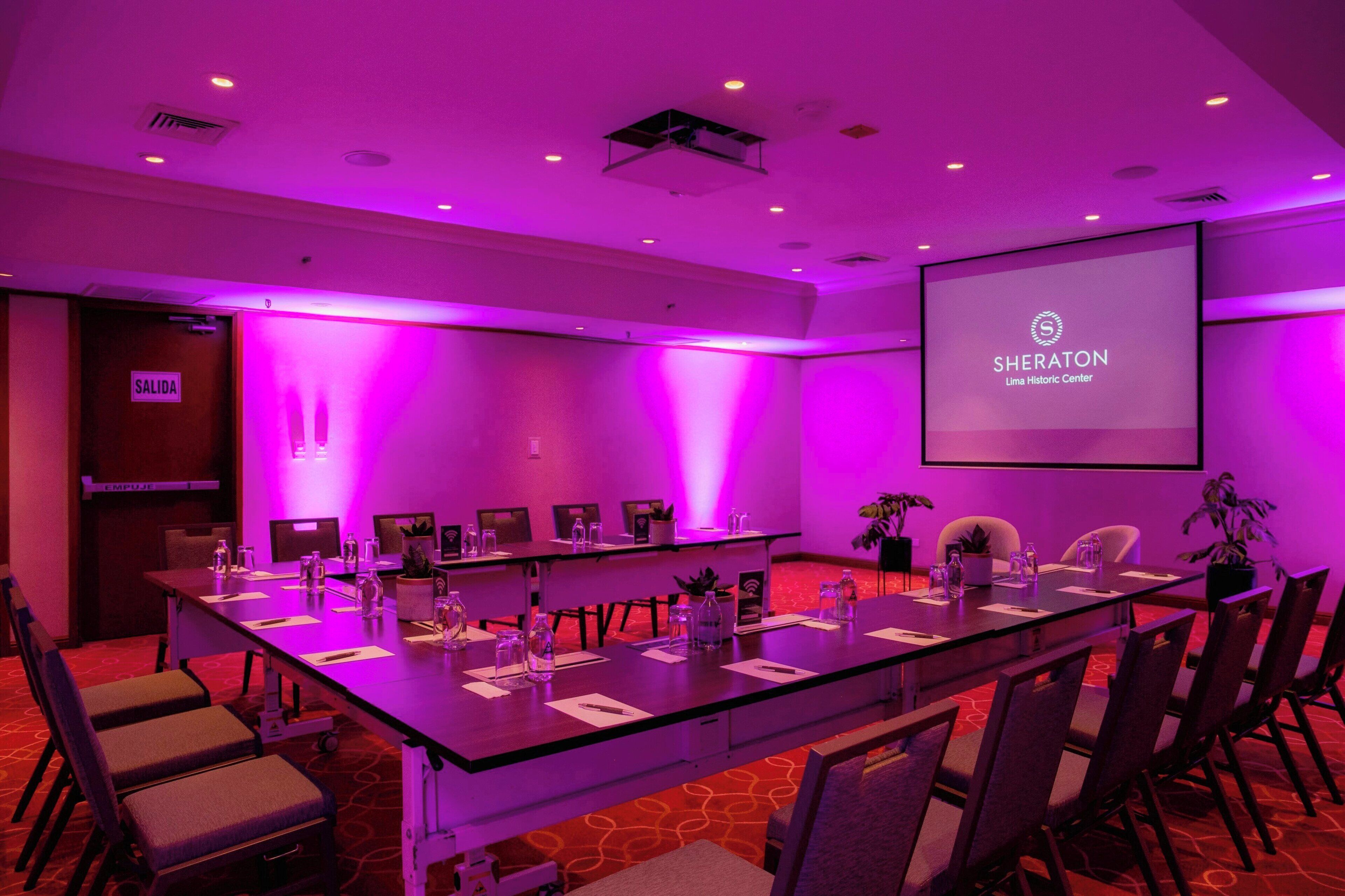 Un salón de conferencias con una larga mesa, sillas y una pantalla que muestra el logotipo de Sheraton.