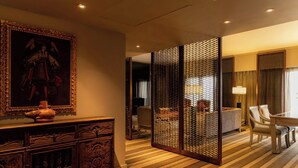 Une chambre d’hôtel avec un meuble traditionnel en bois, un grand tableau encadré, une moquette à rayures et un paravent orné d’un motif tissé.