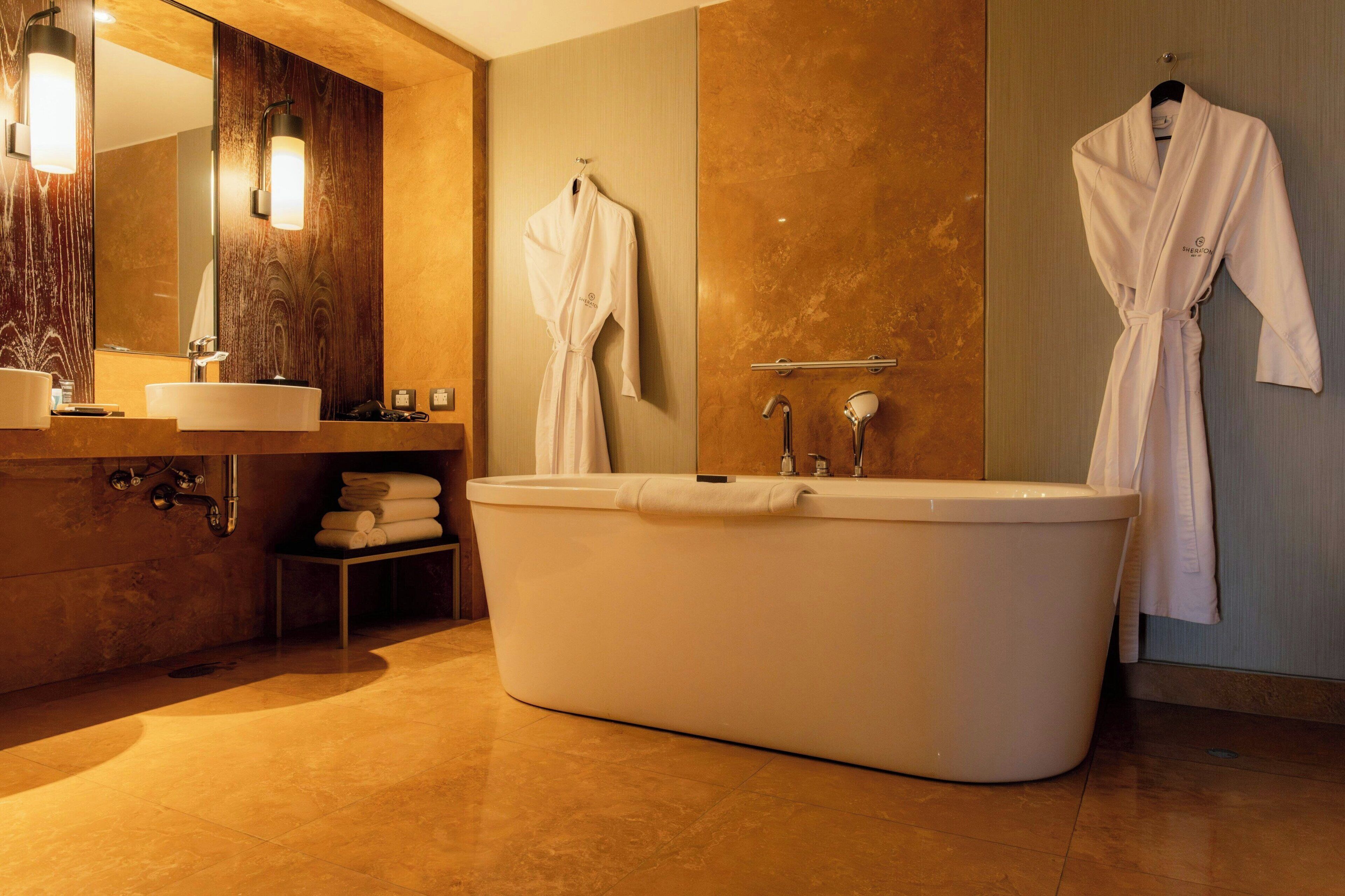 A modern bathroom with a freestanding bathtub, a vanity with a mirror, and two white robes hanging on hooks.