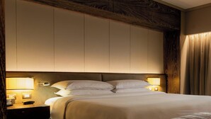 Une chambre d’hôtel avec un grand lit, deux lampes de chevet, une tête de lit en bois et un rideau à la fenêtre.