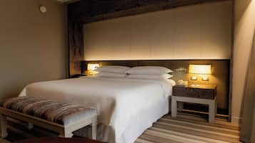 A hotel room with a large bed, bedside lamps, a bench, and a nightstand.