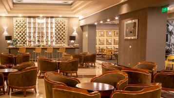 Un hall de hotel con área de bar, disposición de asientos y una pared de fotografías enmarcadas.