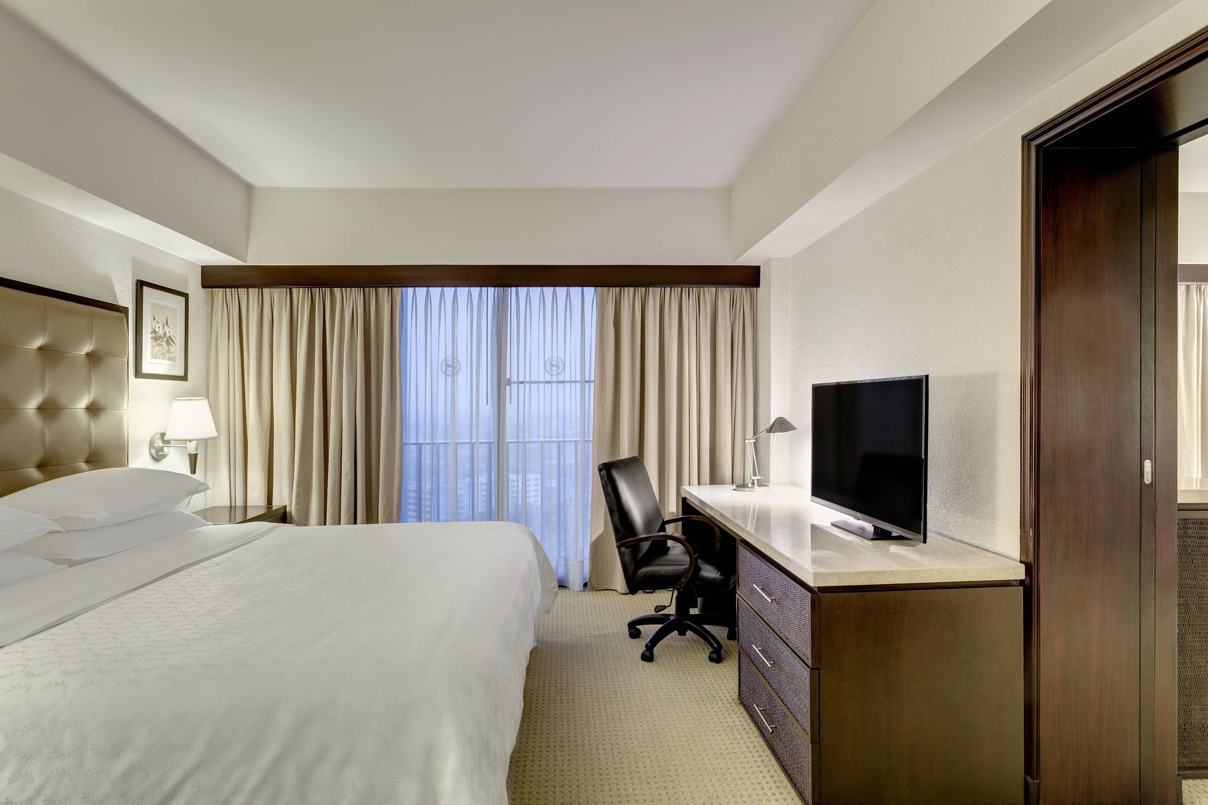 A hotel room with a large bed, a desk with a TV, a chair, and a dresser.