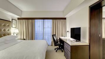 A hotel room with a large bed, a desk with a TV, a chair, and a dresser.