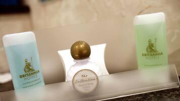 Three toiletries on a hotel counter: a blue bottle labeled 'Britannia Hotels Hair & Body Shampoo', a clear bottle with a gold cap labeled 'The Collection', and a green bottle labeled 'Britannia Hotels Bath & Shower Gel'.