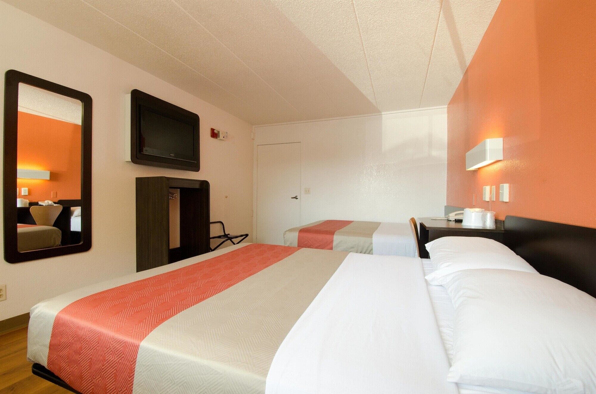 A hotel room with two beds, a TV, a desk with a chair, and a mirror.