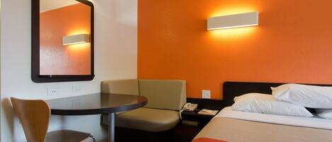 Ein Hotelzimmer mit Bett, Schreibtisch, Stuhl, Nachttisch und einem an der Wand befestigten Spiegel.