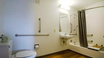 Ein Badezimmer mit Toilette, Waschbecken und Dusche. Es sind Haltegriffe und ein Handlauf vorhanden.