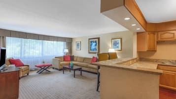 A hotel room with a living area, a sofa, a coffee table, a TV, and a kitchenette.
