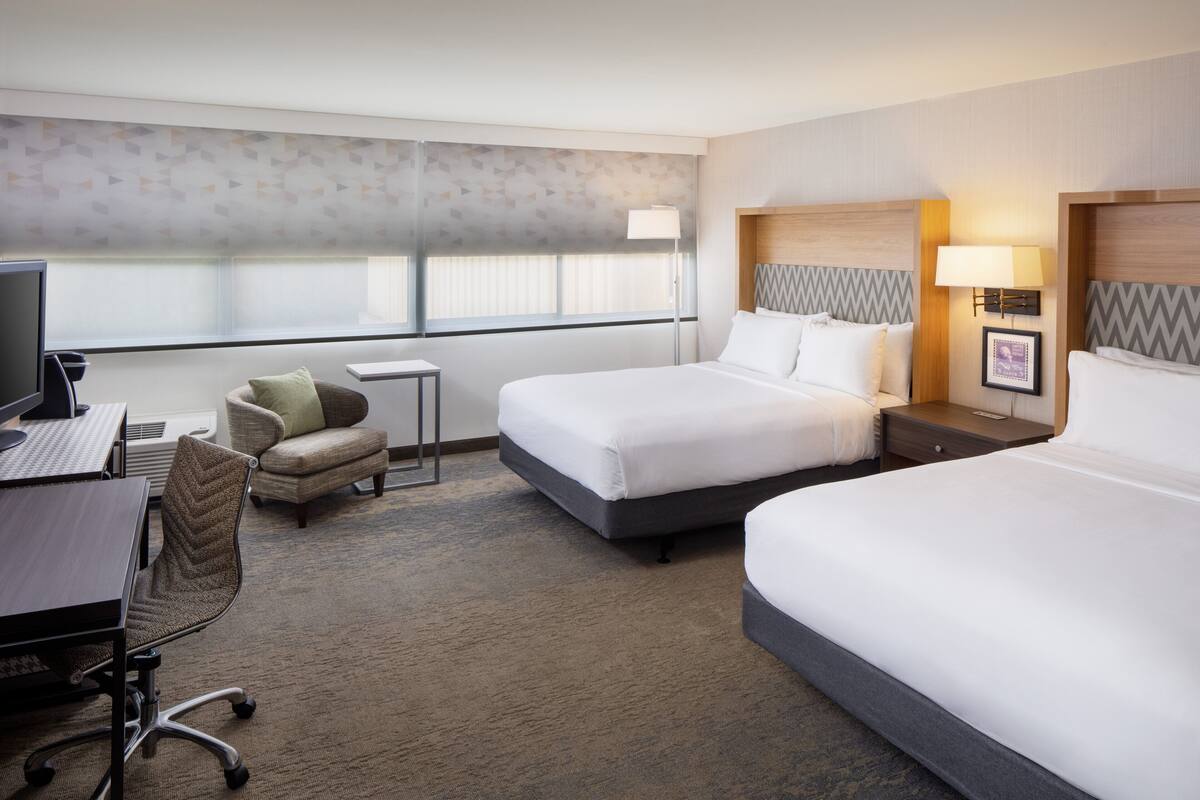 A hotel room with two beds, a desk with a computer, a chair, and a small table.