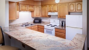 A compact kitchen with wooden cabinets, a microwave, stove, and a refrigerator. - Holiday Inn Charlottesville-Monticello by IHG (Charlottesville)
