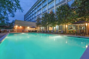 Ein Poolbereich eines Hotels mit klarem Pool, Liegestühlen und einem Gebäude mit zahlreichen Fenstern.