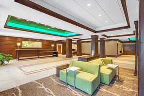 Eine Hotelhalle mit einer Rezeption, einer Sitzecke und einer grün beleuchteten Decke.