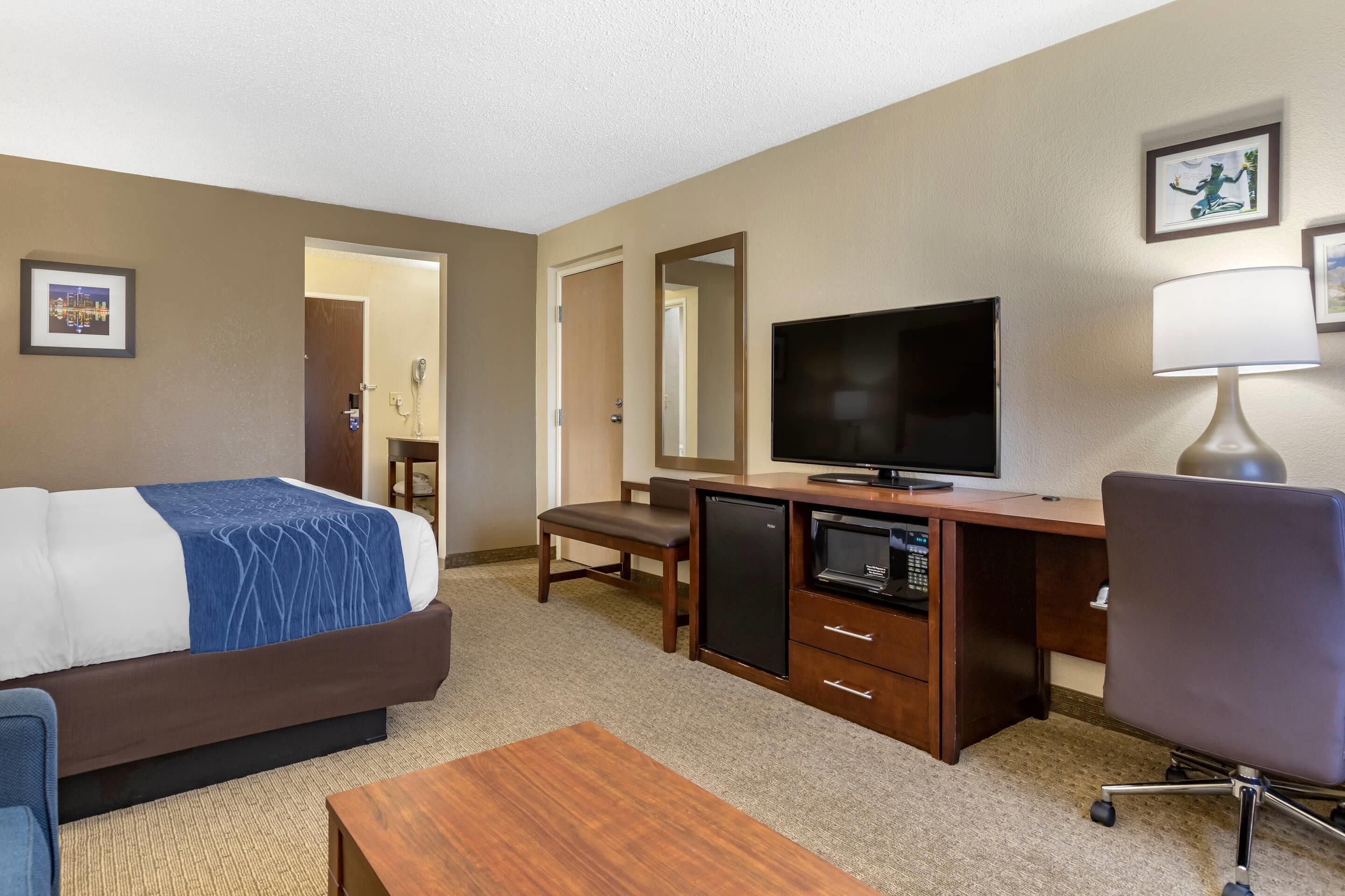 Una habitación de hotel con cama, escritorio, televisor y una silla.