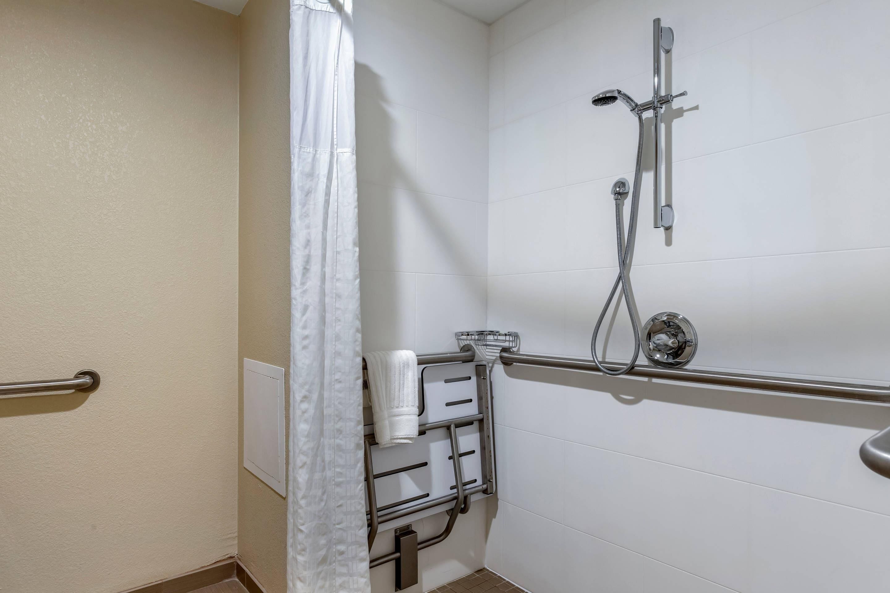 Een badkamer met een douche, handgrepen, een handdoekhouder en een wit gordijn.
