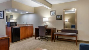 A hotel room with a kitchenette, a desk with a chair, a bench, a mirror, and a lamp. - Comfort Inn Near Greenfield Village (Dearborn)