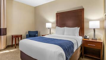 Quarto de hotel com uma cama grande, duas mesas de cabeceira com luminárias, uma mesinha redonda e uma cadeira azul.