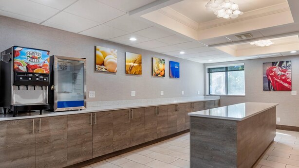 A modern kitchen with a water dispenser, wooden cabinets, a central island, and wall-mounted artwork. - Comfort Inn Near Greenfield Village (Dearborn)