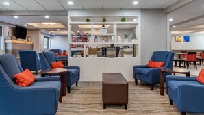 A modern hotel lobby with blue armchairs, a central brown ottoman, and a display of decorative items. - Comfort Inn Near Greenfield Village (Dearborn)
