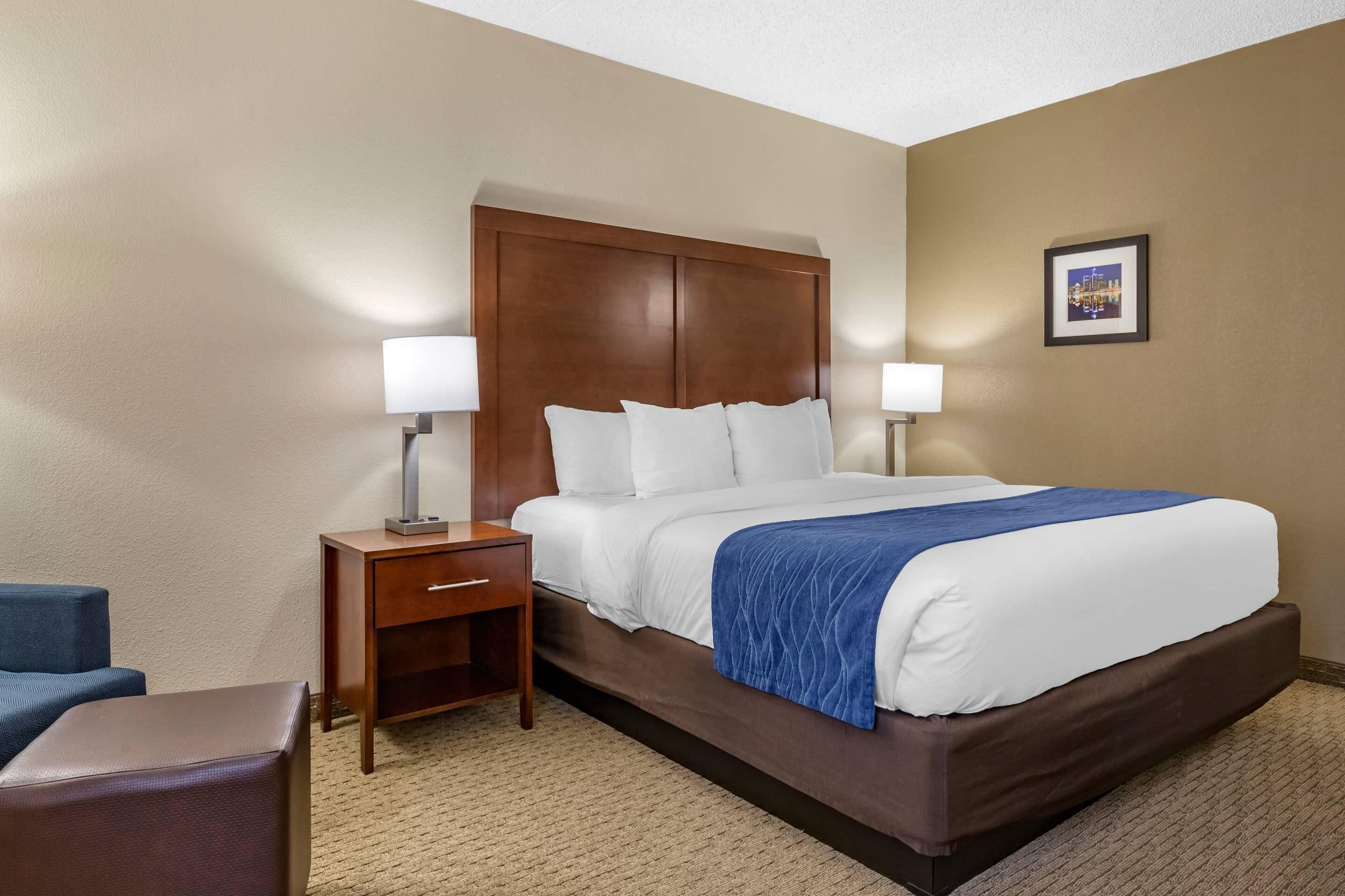 A hotel room with a bed, two bedside tables with lamps, a chair, and a carpeted floor.