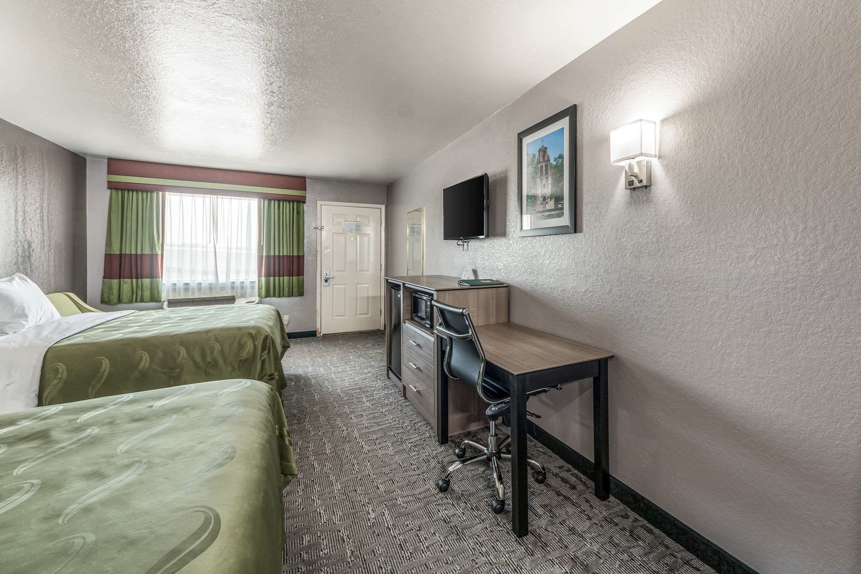 A hotel room with two beds, a desk, a chair, a television, and a window with curtains.