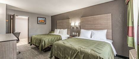Habitación de hotel con dos camas, un escritorio y una silla. Se ve una puerta que conduce a otra habitación y una lámpara fijada a la pared.