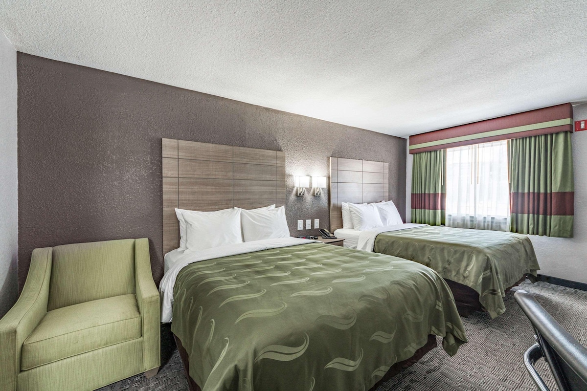 Een hotelkamer met twee bedden, een groene fauteuil, een hoofdbord en een raam met gordijnen.