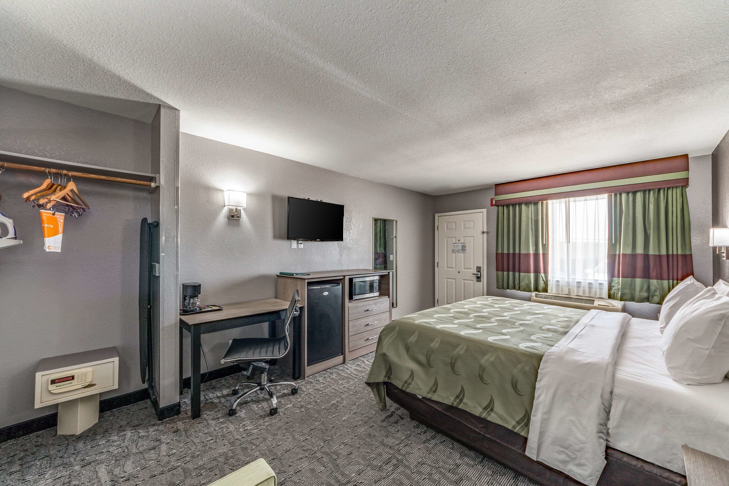 A hotel room with a bed, desk, chair, television, and a window with curtains.