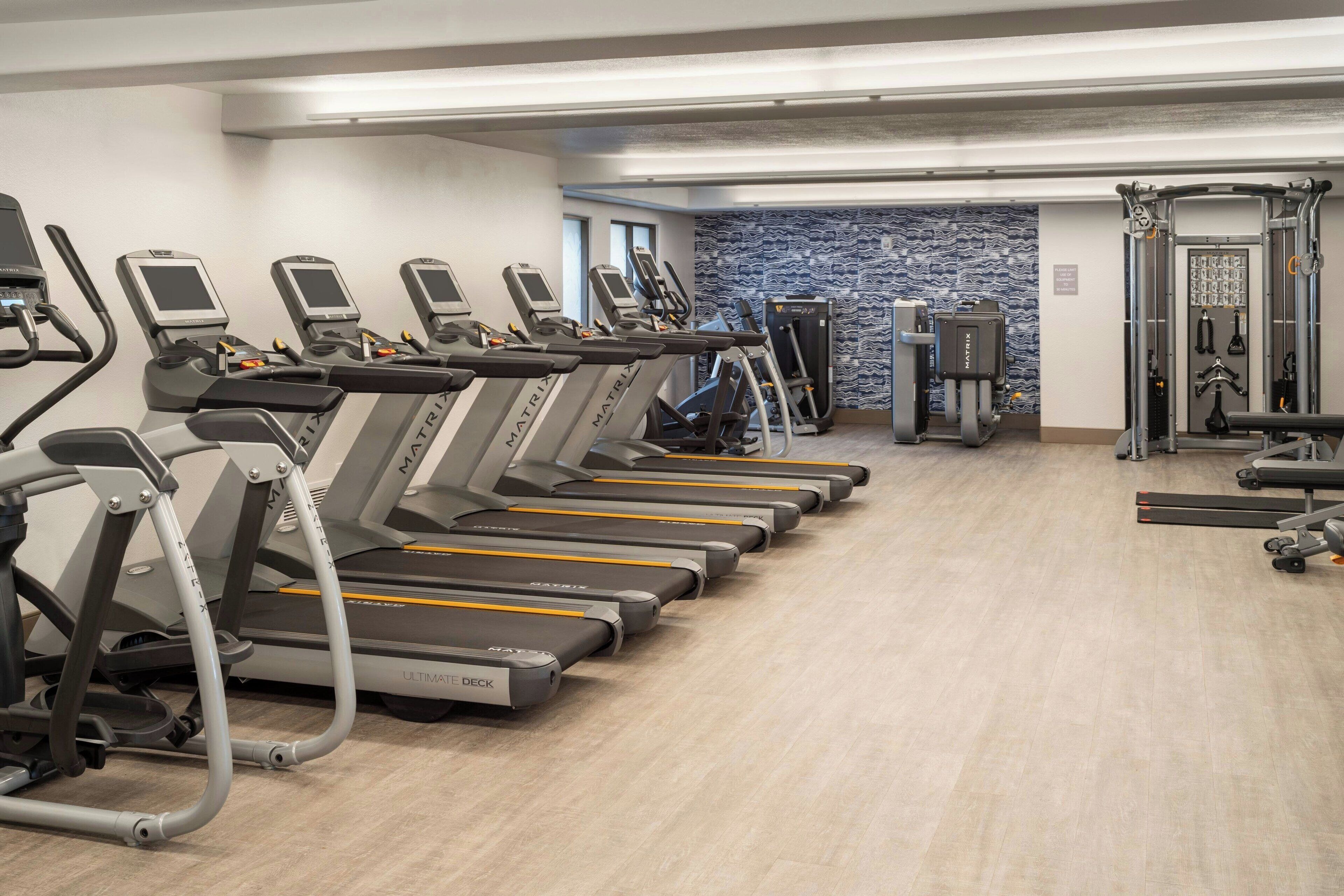 A gym with multiple treadmills, a weightlifting area, and a patterned wall.