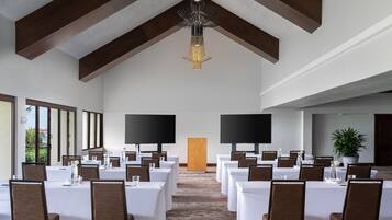 Un salón de conferencias con mesas y sillas, una lámpara de araña grande y una planta.