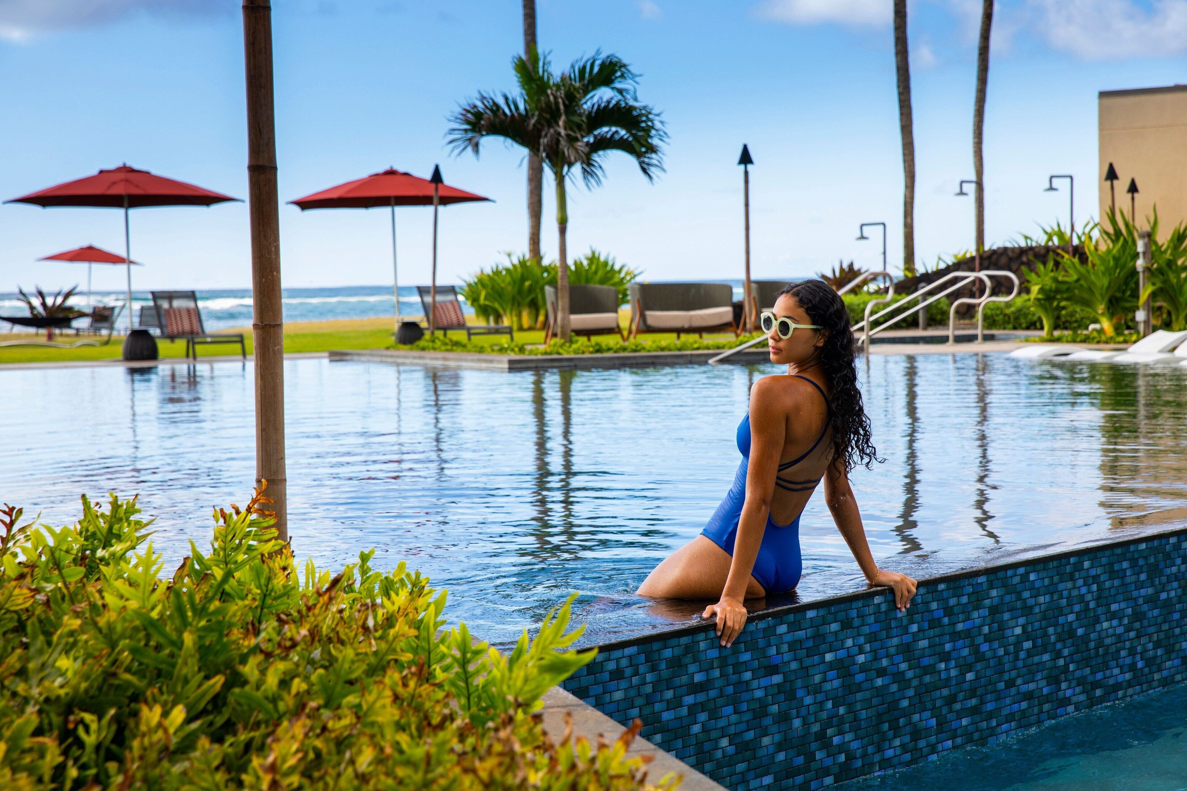 A poolside area with a view of the ocean, lounge chairs, and umbrellas.
