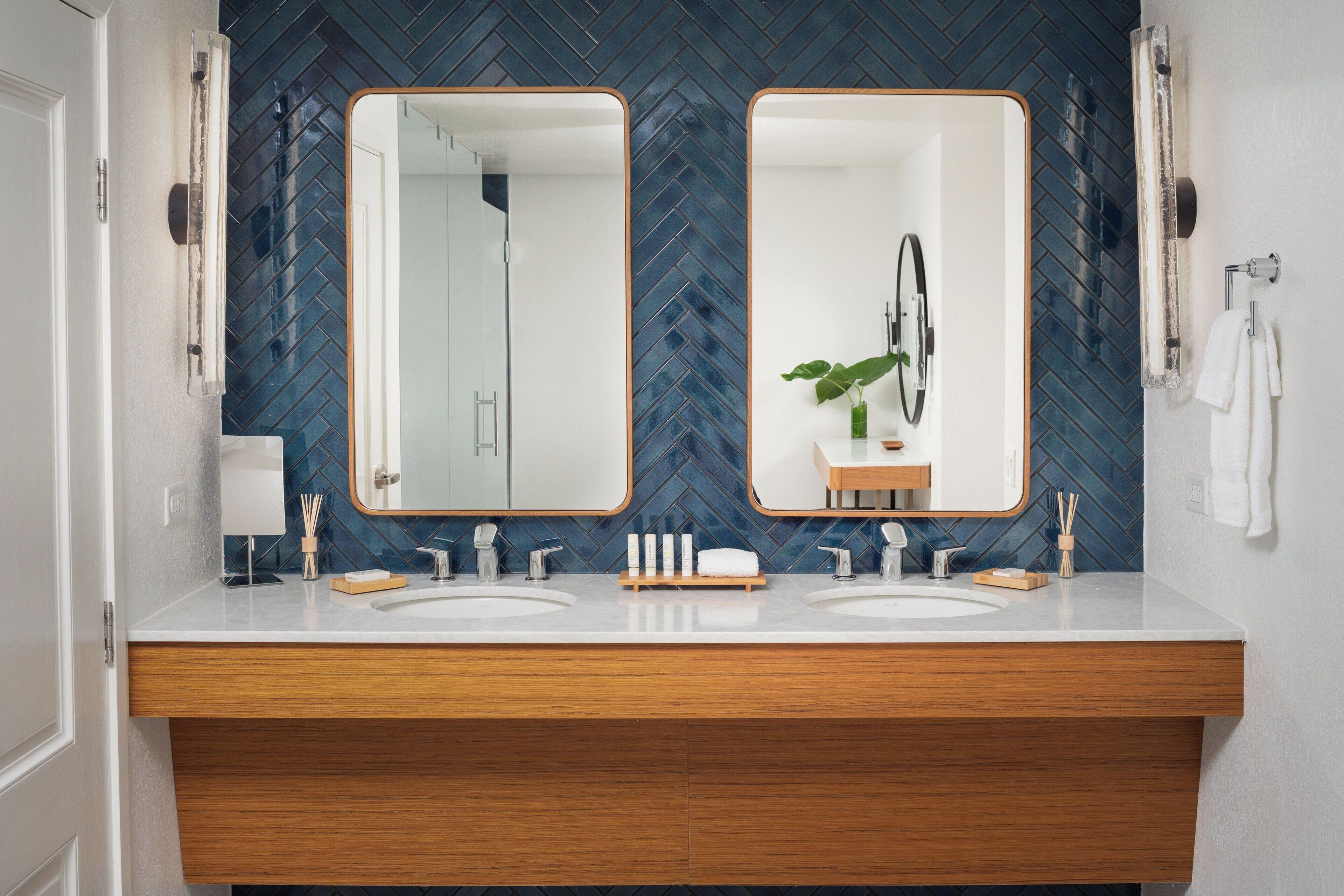 A bathroom with two sinks, wooden vanity, mirrored cabinets, and a blue herringbone tile backsplash.