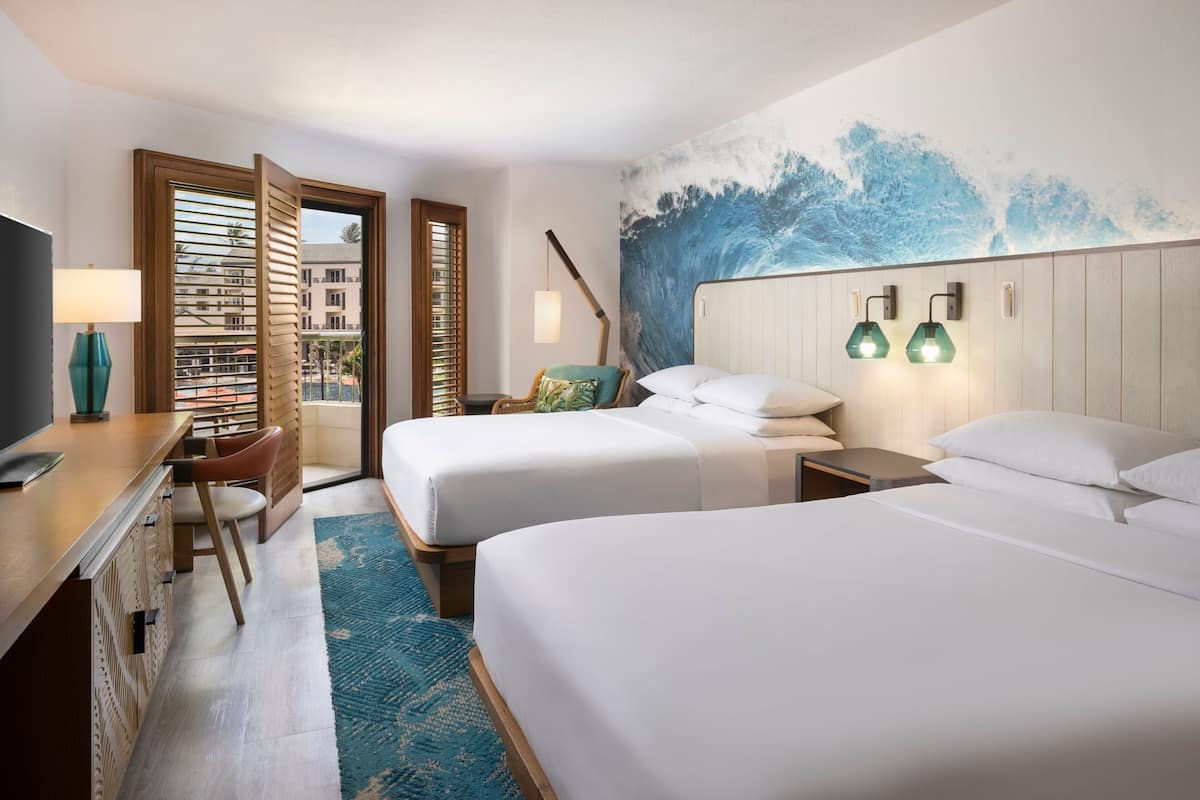 A hotel room with two beds, a desk with a TV, a chair, a window with blinds, and a wall mural.