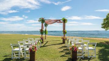 A beach ceremony setup with white chairs and a floral arch.