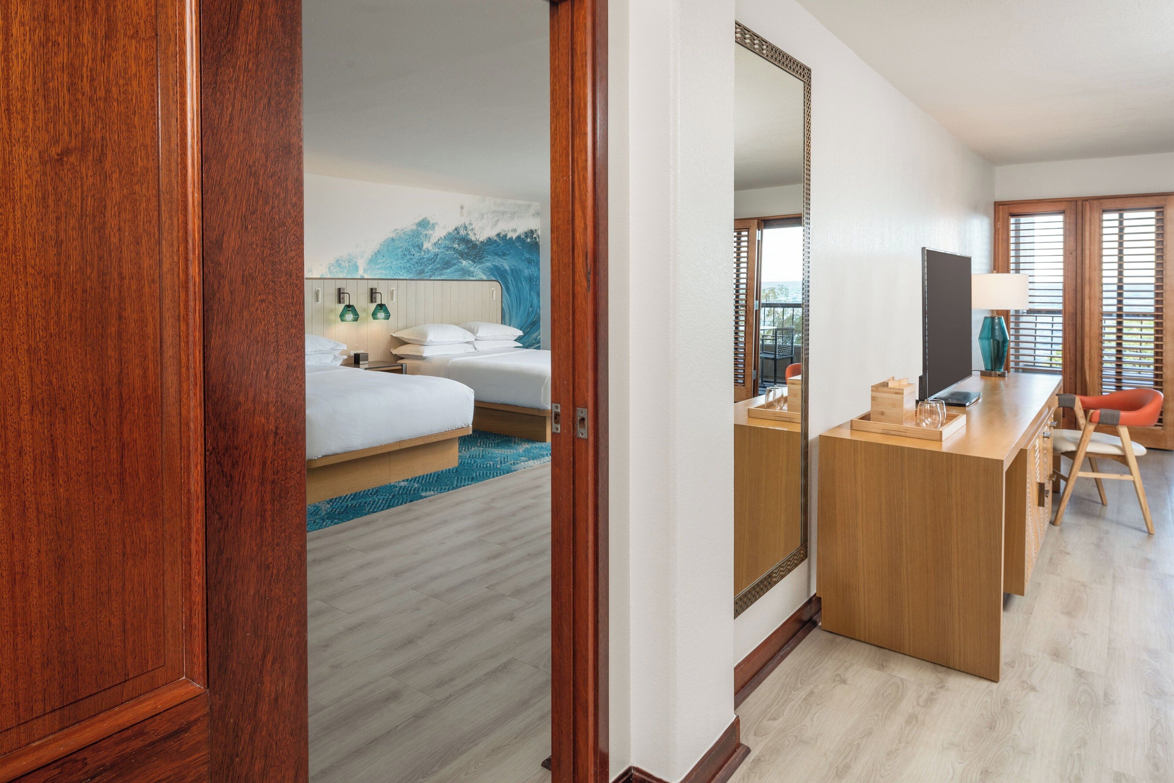 A hotel room with a wooden desk, a bed with white linens, and a large mirror.