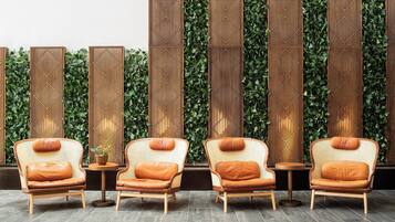 A seating area with wicker chairs and a small table, set against a backdrop of vertical wooden panels and green foliage.