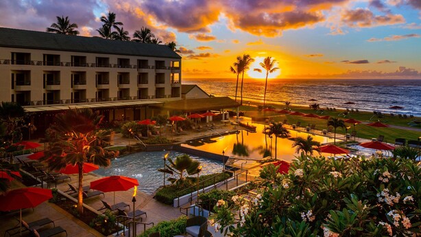 A resort with a pool, outdoor seating, and a view of the sunset over the ocean. - Sheraton Kauai Coconut Beach Resort (Kapaa)