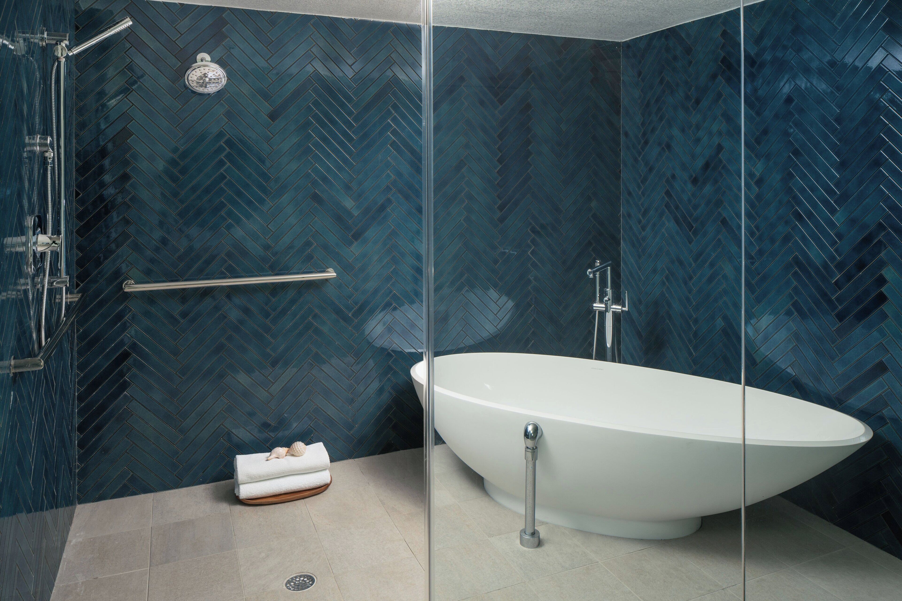 A modern bathroom with a freestanding bathtub, a glass shower enclosure, and a herringbone-patterned tile wall.