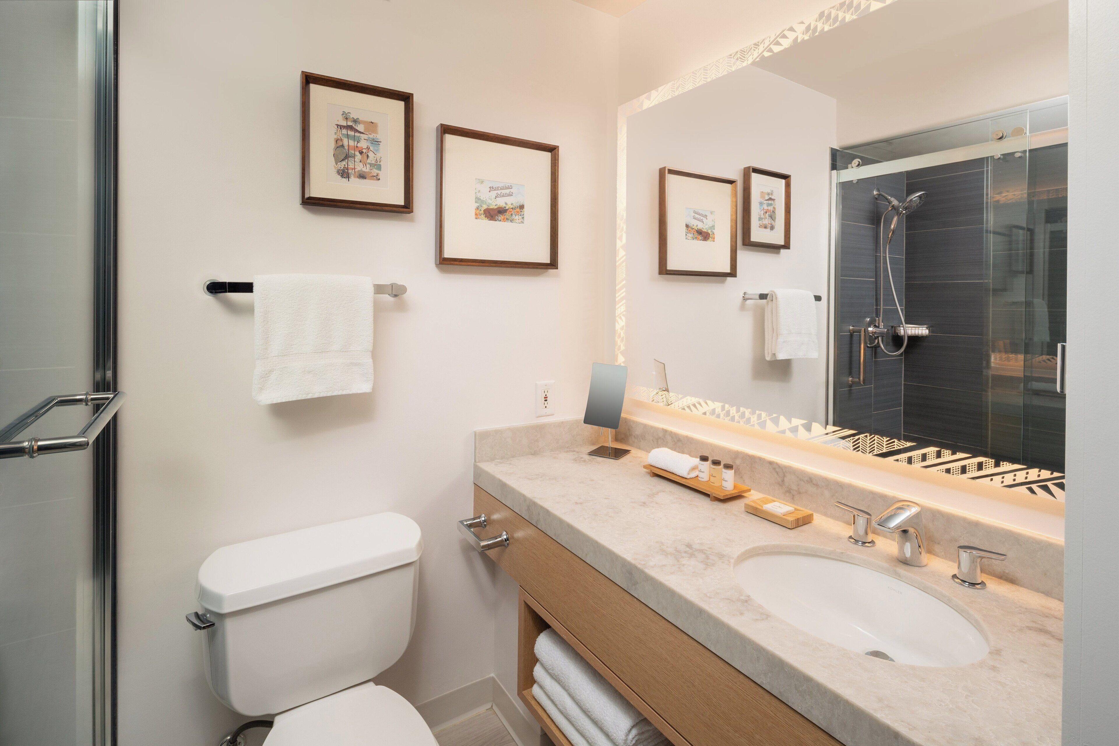 A modern bathroom with a toilet, sink, and shower. There are framed pictures on the wall and a towel rack.