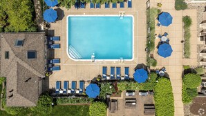 Vista aérea de uma área de piscina com uma piscina retangular, cadeiras de sol e guarda-sóis.