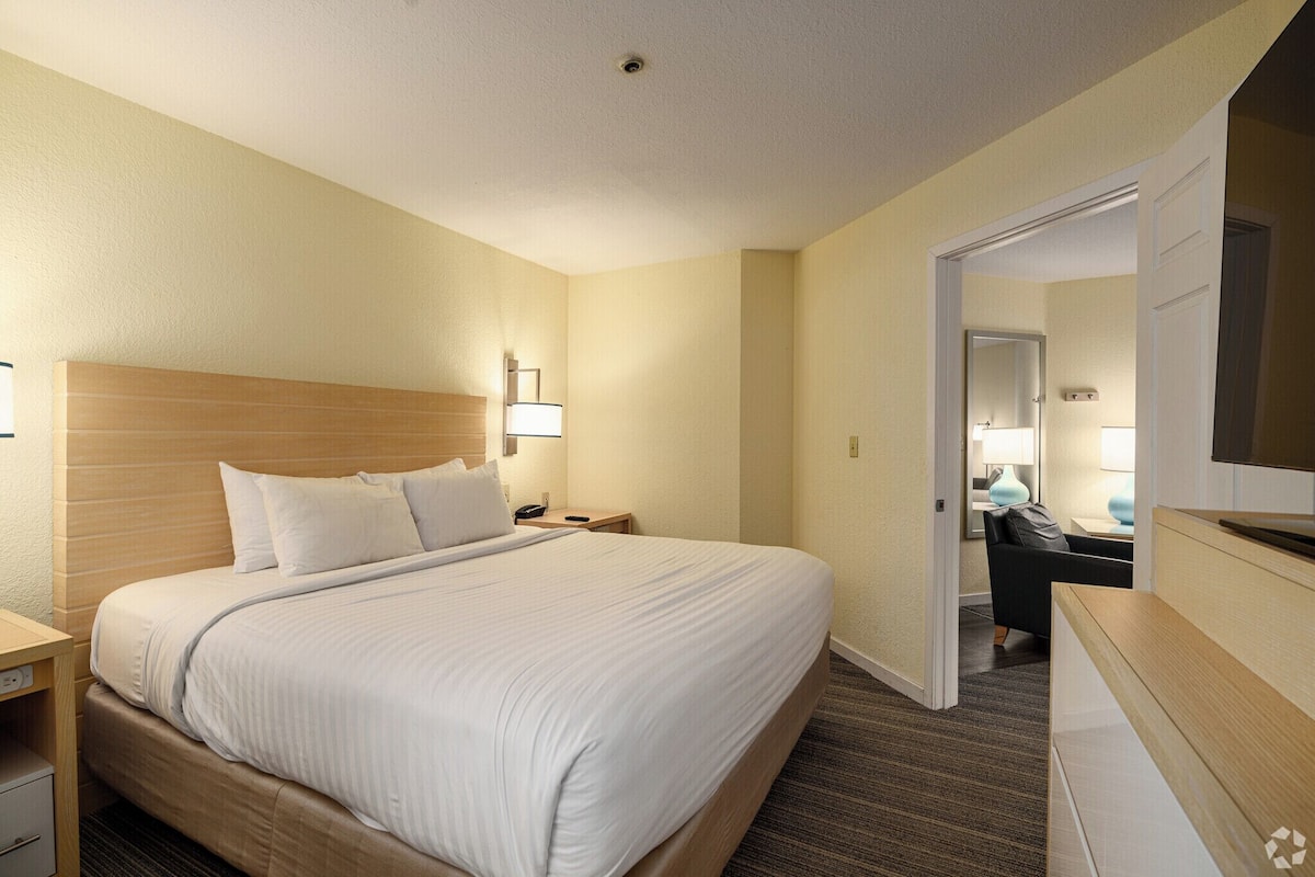 A hotel room with a large bed, bedside tables, a desk with a chair, and a mirror.