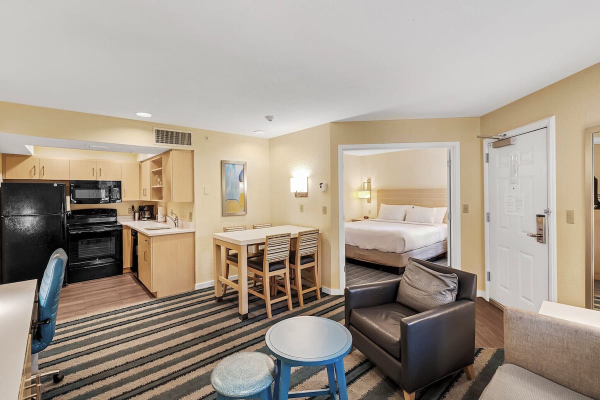 A compact hotel room with a kitchenette, a dining area, a sofa, and a bed.